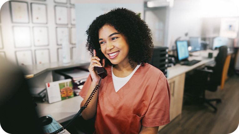 Nurse wearing orange scrubs smiling while on the phone Nurse wearing orange scrubs smiling while on the phone