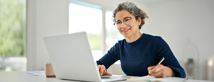 Woman wearing a blue shirt writing while smiling at her laptop Woman wearing a blue shirt writing while smiling at her laptop